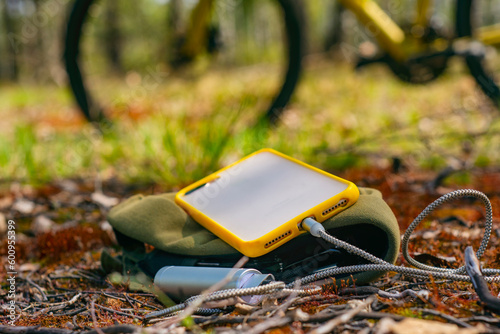 A portable charger charges the smartphone. Power Bank with cable against the background on the forest and bicycle.