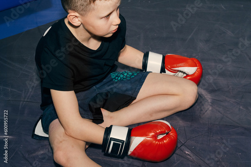 Close-up of a teenager boy in boxing gloves sitting in the ring after training