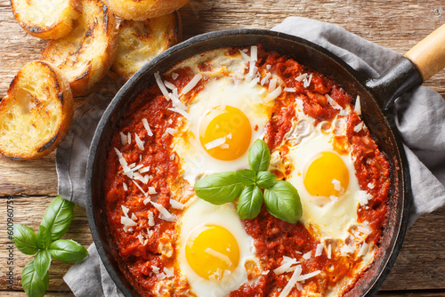 Eggs in purgatory with tomato basil garlic sauce and a sprinkling of Parmesan closeup on the skillet on the wooden table. Horizontal top view from above