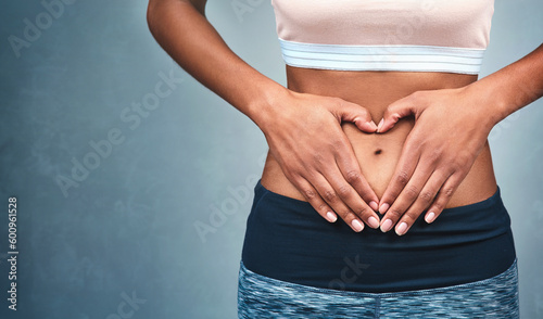 Heart, fitness and hands of a woman on a stomach isolated on a dark background in studio. Wellness, gut health and a girl with shape for love of body, weight loss and abdomen digestion on backdrop photo