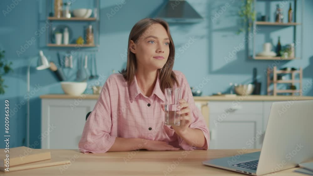 Freelance Young Woman Drink a Glass of Clean Water in Kitchen. Smiling Woman Start New Day with Healthy Life Habit, Holding Glass Drinking Clean Mineral Natural Water. Lifestyle Healthcare Concept. Freelance Young Woman Drink a Glass of Clean Water in Kitchen. Smiling Woman Start New Day with Healthy Life Habit, Holding Glass Drinking Clean Mineral Natural Water. Lifestyle Healthcare Concept.