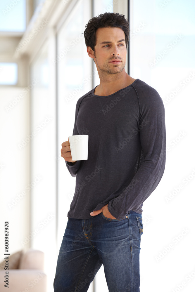 Handsome, young and man with a cup of coffee standing by the window in a vacation house. Calm, relax and attractive male person drinking a capuccino in the living room while thinking or daydreaming. Handsome, young and man with a cup of coffee standing by the window in a vacation house. Calm, relax and attractive male person drinking a capuccino in the living room while thinking or daydreaming.