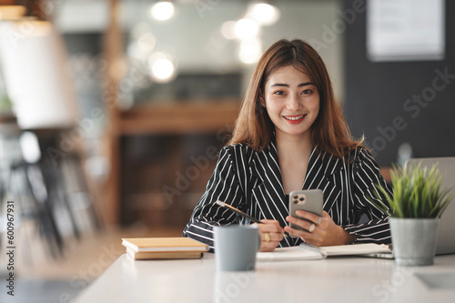 Happy businesswoman using mobile phone while analyzing weekly schedule in her notebook.