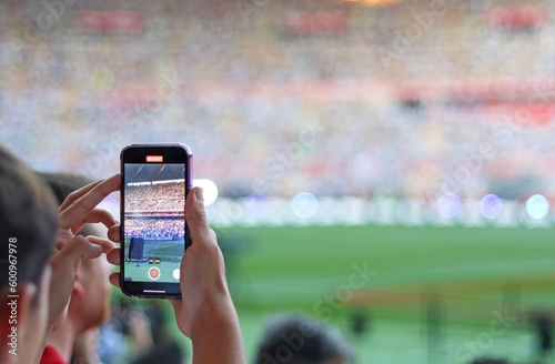 A fan recording a football match from the stands with his mobile phone. Selective focus. 