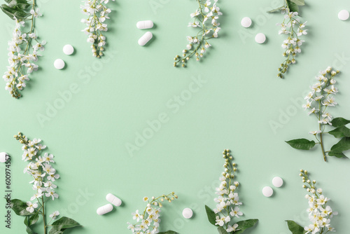 Seasonal spring allergies, fresh spring blooming branches tree and up white pills on green background with copy space, top view, minimal flat lay frame, Seasonal allergy treatment concept © yrabota