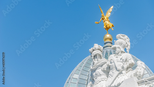 Dresden, Germany - May 3, 2023: Banner with old statue of a golden angel and warriors and knights at the dome top in downtown of Dresden, with copy space blue sky solid background.