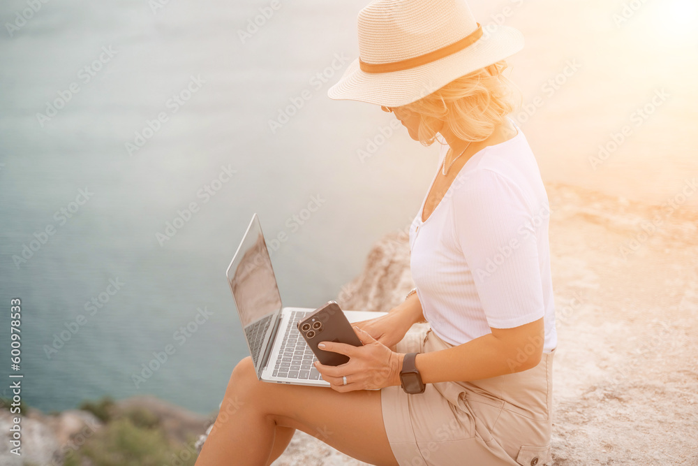 Freelance women sea working on the computer. Good looking middle aged woman typing on a laptop keyboard outdoors with a beautiful sea view. The concept of remote work.