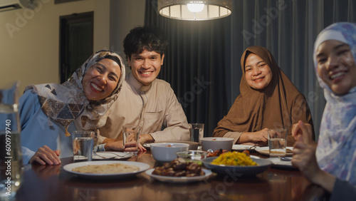 Happy Asian muslim family celebrate long distance with cousin looking at camera video call online Ramadan dinner together at home. Two generation celebration of Eid al-Fitr togetherness at home.