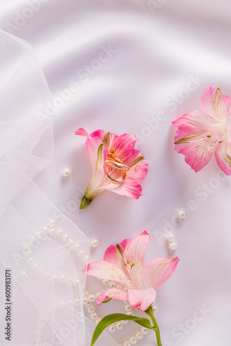 A pair of beautiful gold wedding rings lie in an astromeria flower bud on a white satin background with a piece of veil. postcard. invitation. photo