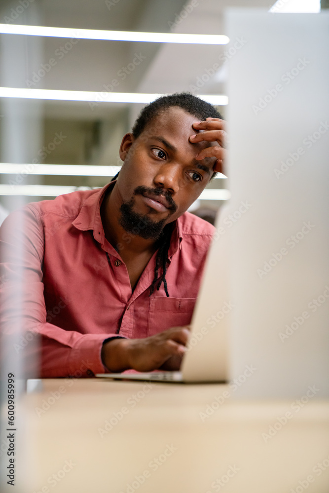 Naklejka premium Stressful job. Stressed african businessman working at laptop, having problem at workplace.