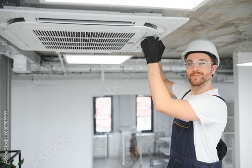 Young repairman repairing ceiling air conditioning unit