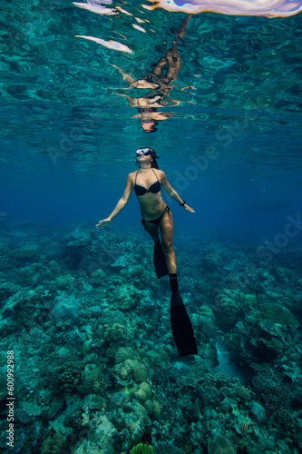 Young Asian woman in bikini swims in tropical waters above coral reef