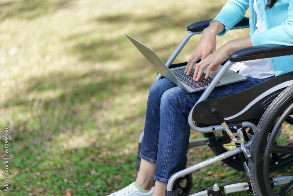 Obraz premium Young asian woman in wheelchair working with laptop