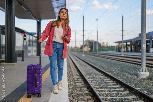 Adult woman is standing at railway station and waiting for arrival of train.