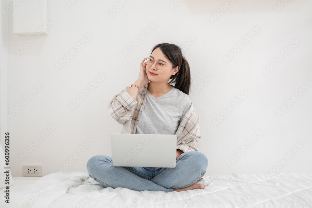 Asian freelance woman using the laptop sitting on the bed in the room Asian freelance woman using the laptop sitting on the bed in the room