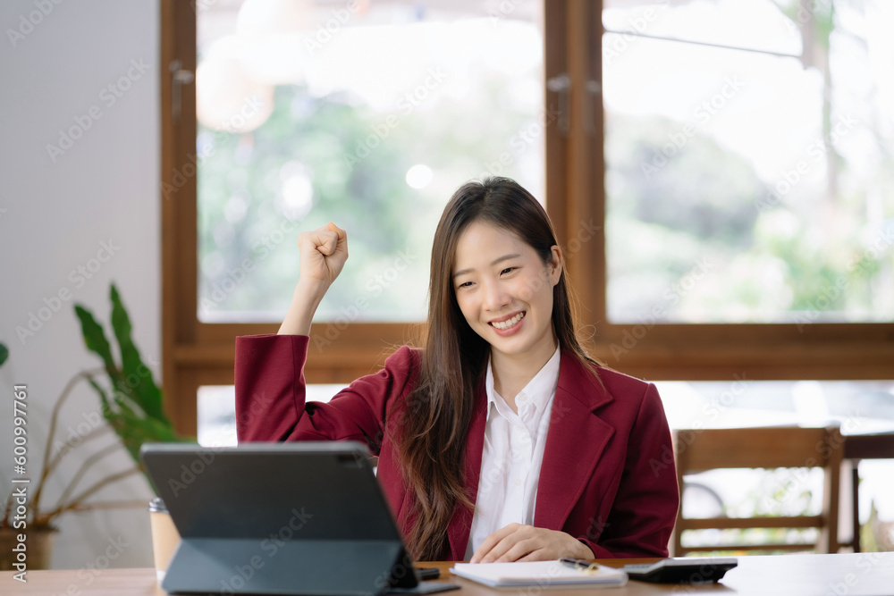 Smiling young asian woman succeeding in business using laptop and computer while doing some paperwork at office.