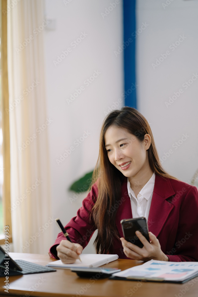 Businesswoman hand working at a tablet, computer and writing on a notepad with a pen in the office. on the wooden desk there a graph business diagram.