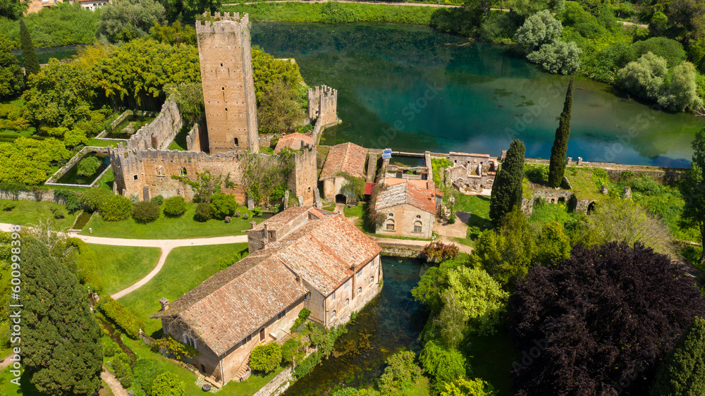 Aerial view of the ruins of the castle and tower located in the garden of Ninfa, near Latina, Italy. The park is an Italian natural monument and contains a lake and a river. It is empty. Aerial view of the ruins of the castle and tower located in the garden of Ninfa, near Latina, Italy. The park is an Italian natural monument and contains a lake and a river. It is empty.