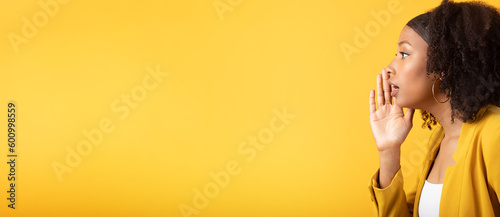 Black lady whispering secret, pressing hand to face, isolated on yellow background, side view, panorama with free space