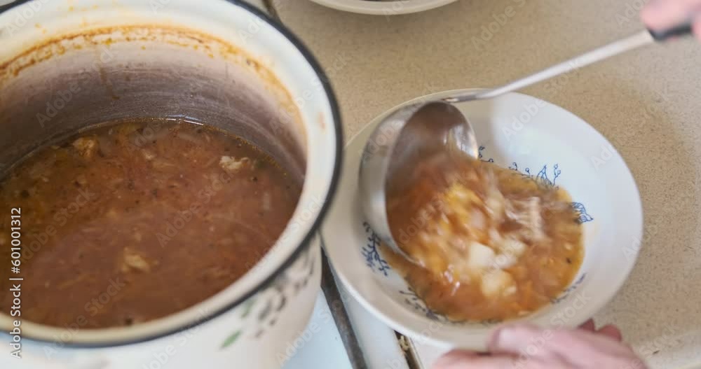 Man's hand pours soup into plate from saucepan with ladle. Top view, close-up. Warming up dinner at home for an elderly single man. Man's hand pours soup into plate from saucepan with ladle. Top view, close-up. Warming up dinner at home for an elderly single man.