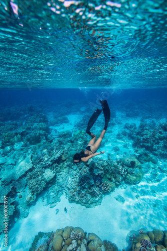 A young woman in bikini free dives above a coral reef in clear tropical water