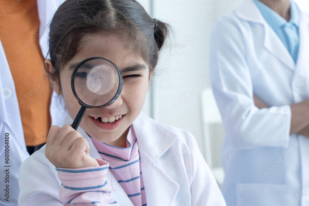 Naklejka premium Little girl wearing lab coat for learning in laboratory at school holding a magnifying glass to cover her face