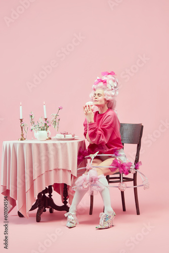 Portrait gorgeous hungry queen wearing big pink wig holding marshmallow with exciting face on pink studio background. Yummy cake