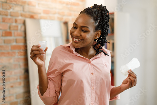Discovering personal period preferences. Happy young black woman holding menstrual cup and sanitary pad in her hands photo