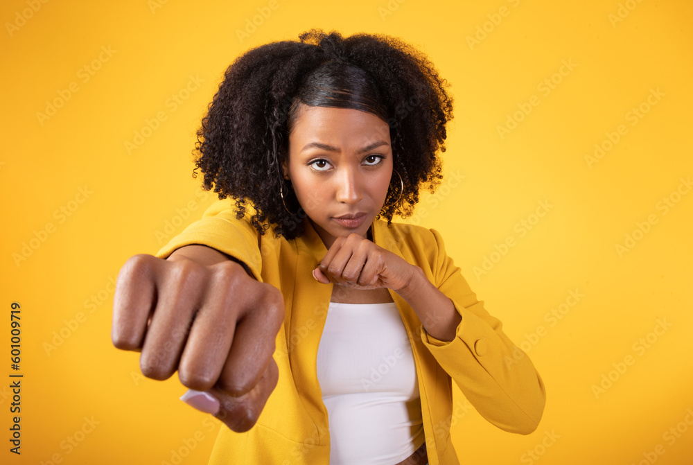 Serious black curly lady doing hand punch, standing on yellow background, closeup studio shot, copy space