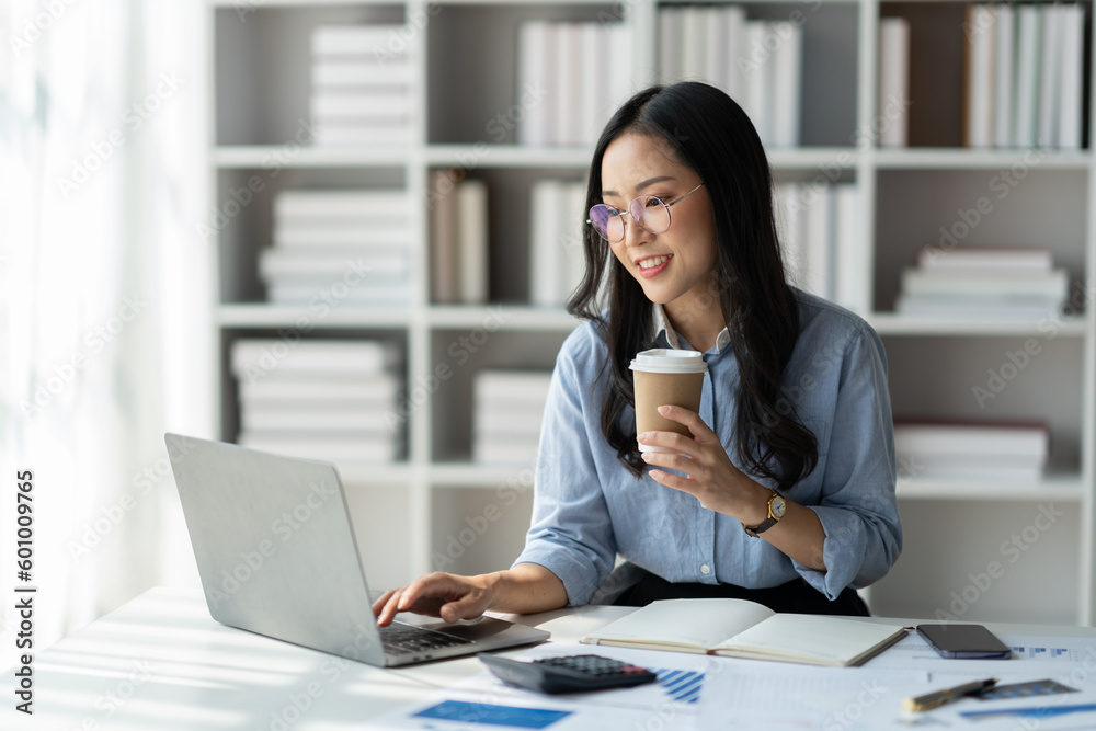 Modern working lifestyle, asian businesswoman sitting and holding coffee cup Break to relax at desk with laptop online using internet happy in office. Modern working lifestyle, asian businesswoman sitting and holding coffee cup Break to relax at desk with laptop online using internet happy in office.
