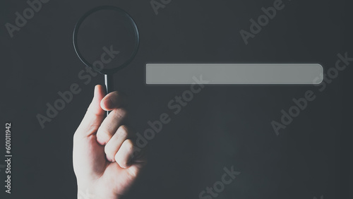 Search Engine Optimization, Search bar on virtual screen with hand holding magnifying glass.