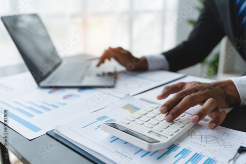 Confident businessman analyzing Calculate and view chart data from documents. financial report graph from laptop computer on office desk.