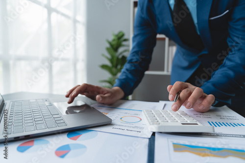 Confident businessman analyzing Calculate and view chart data from documents. financial report graph from laptop computer on office desk.