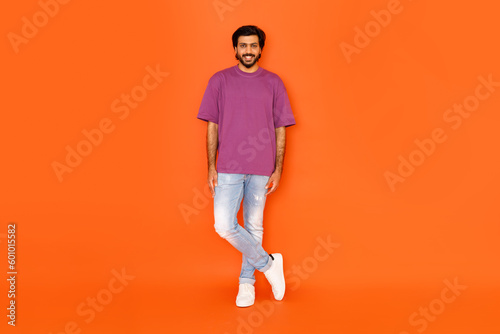 Stylish positive hindu guy posing on orange studio background