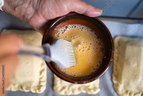 top view of woman hands dipping a pastry brush on beaten egg to cover dumplings