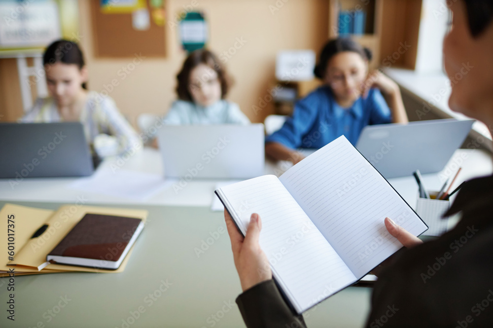 Close-up of teacher opening her notebook and giving homework to children during lesson