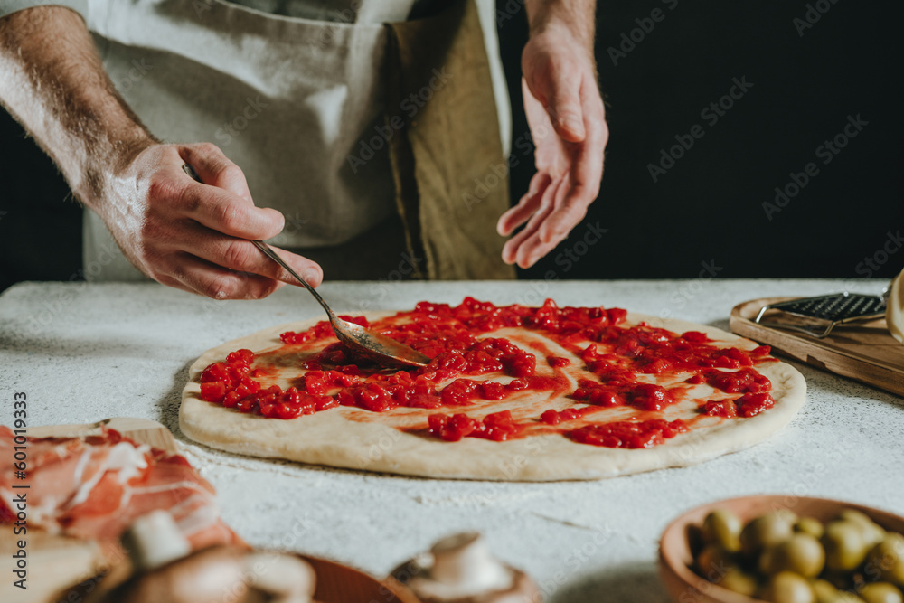 Close-up of chef preparing pizza putting tomato sauce on the dough
