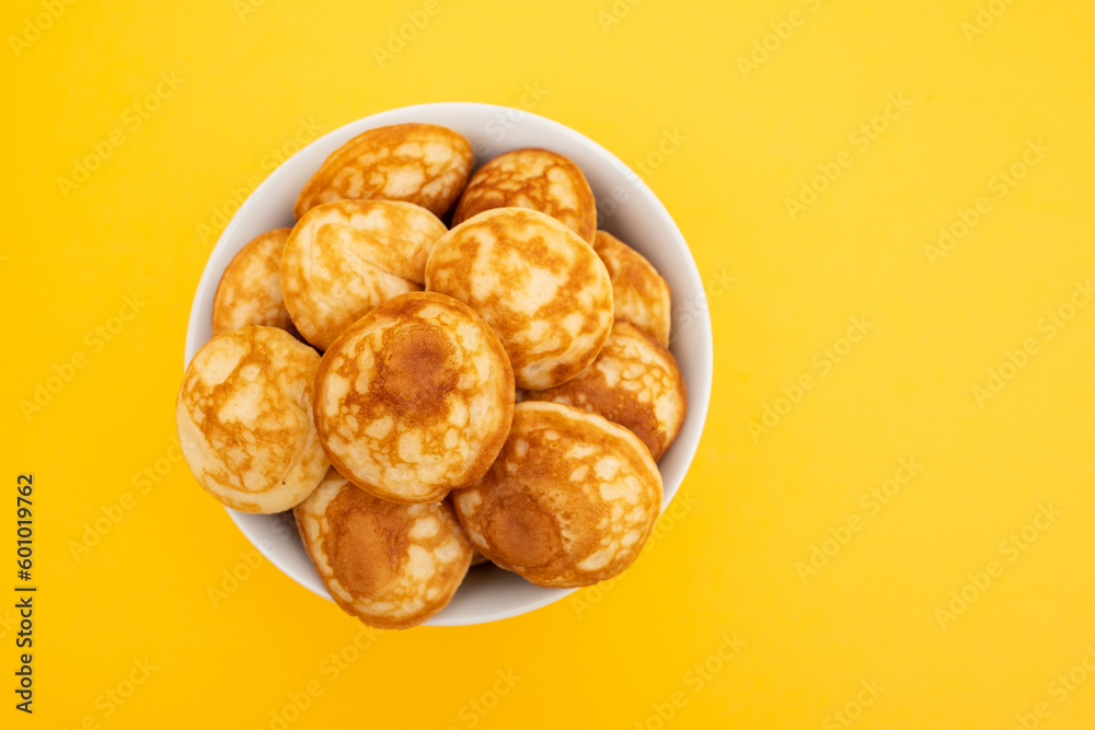 Heap of mini cereal pancakes in bowl on bright background.