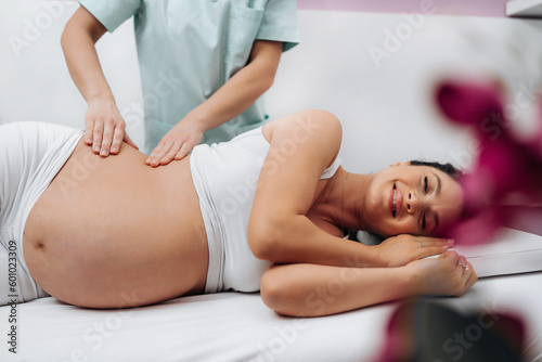 Beautiful young pregnant woman enjoying and relaxing during special massage treatment for maintaining healthy pregnancy.