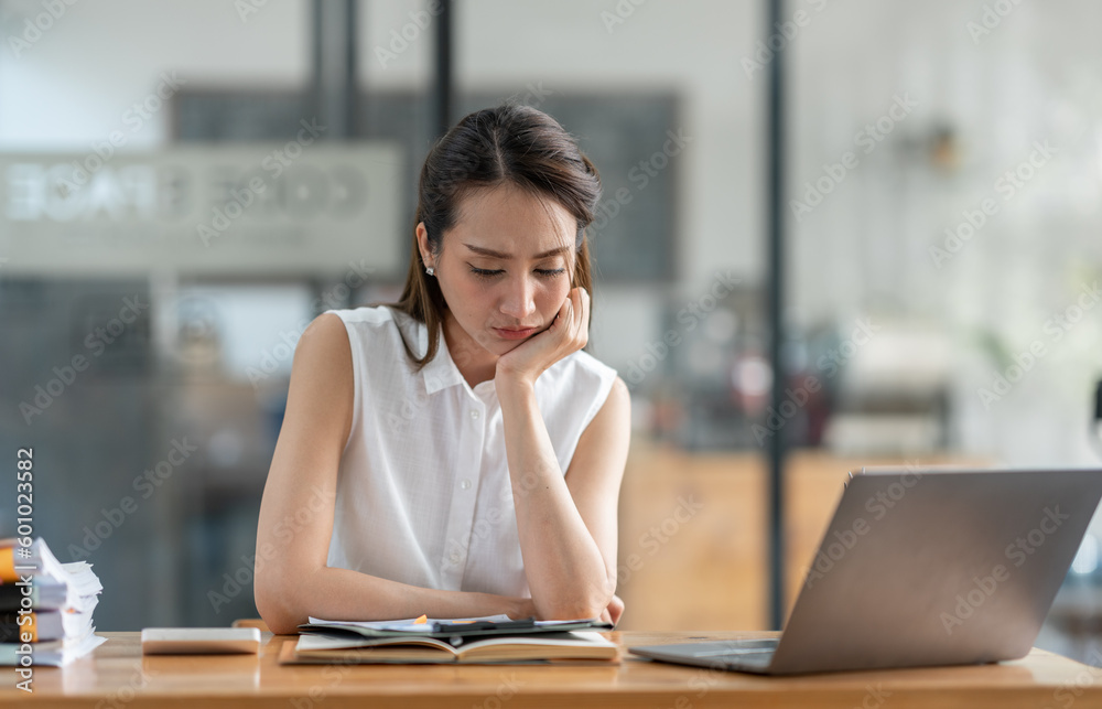 Young Asian businesswomen sit stressed out solving various parts of the financial business tasks. administration at her office. Young Asian businesswomen sit stressed out solving various parts of the financial business tasks. administration at her office.