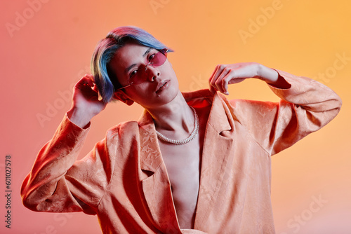 Portrait of stylish dancer in pink sunglasses posing at camera against colored neon background