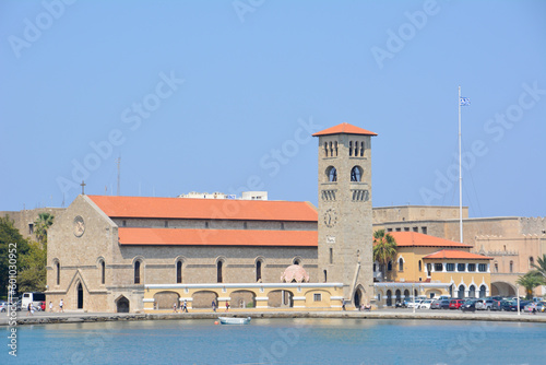 A large building with red roof and a tower clock and waterfront with mediterranean sea, mandraki