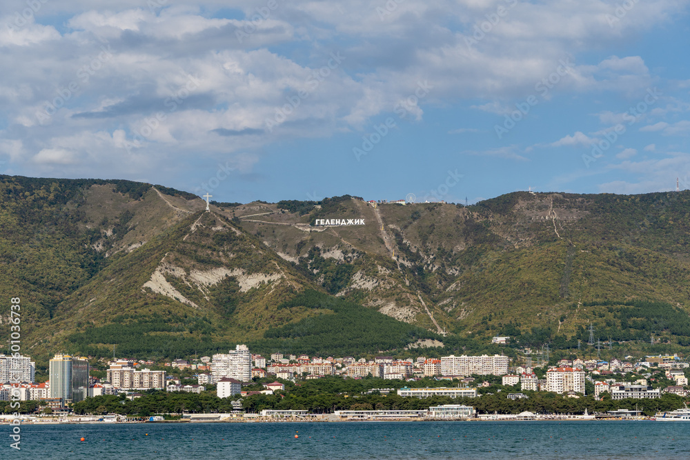 Gelendzhik bay. View of city. In background coastline with hotels and boarding houses. On mountains there is Orthodox cross and inscription Gelendzhik. Gelendzhik, Russia - September 19, 2022