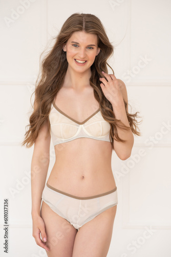 Confident beautiful young woman posing on white background at home in comfortable underwear smiling and looking away.