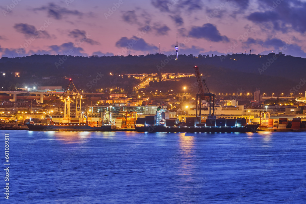 View of Lisbon port with sea container ships with port cranes in the evening twilight over Tagus river. Lisbon, Portugal