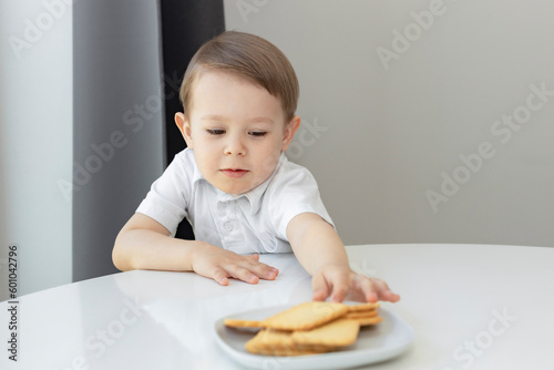 Cute little boy stealing delicious  cookies  on table, child  try to take homemade cookies from plate, unhealthy food and kids sugar  addiction concept