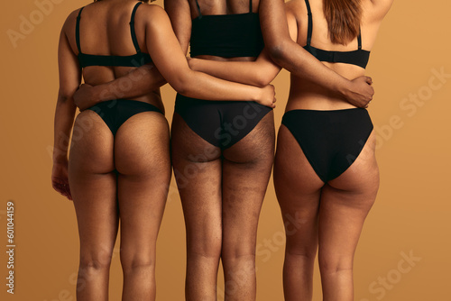Crop multiracial women with stretch marks hugging in studio