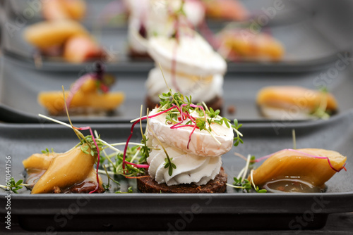 Appetizer dish from savory cream and goat cheese on pumpernickel bread with rhubarb pieces and sprout garnish served on black plates, selected focus photo