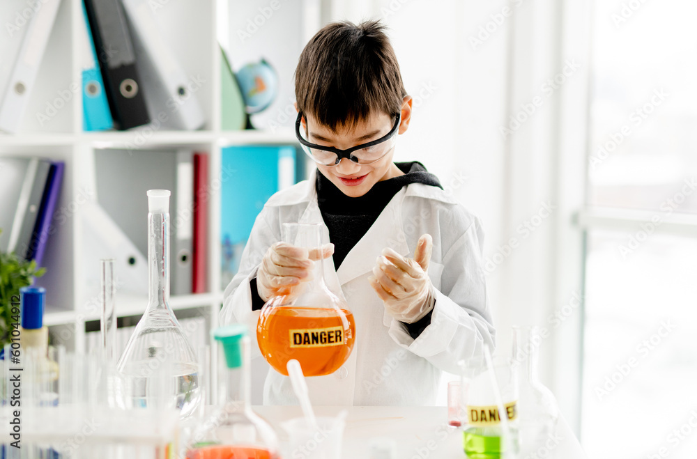School boy wearing protection glasses doing chemistry experiment in elementary science class. Clever pupil holding tube with danger mark in lab during test School boy wearing protection glasses doing chemistry experiment in elementary science class. Clever pupil holding tube with danger mark in lab during test