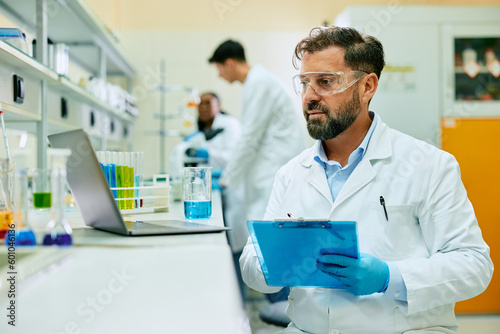 Male scientist taking notes while analyzing medical data on laptop in laboratory.